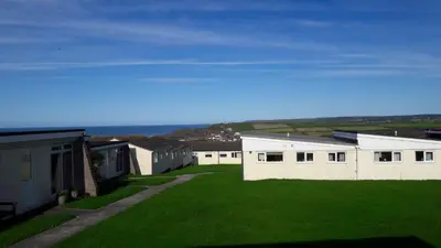 a row of white buildings with a grass yard at Chalet 18 Widemouth Bay Holiday Village in Bude