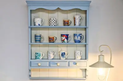a shelf filled with cups and mugs next to a lamp at BY THE BEACH Harlyn Bay in St Merryn