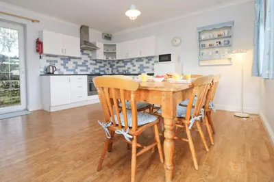 a kitchen and dining room with a wooden table and chairs at BY THE BEACH Harlyn Bay in St Merryn