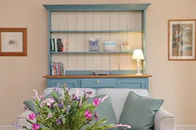 a living room with a couch and a book shelf at BY THE BEACH Harlyn Bay in St Merryn