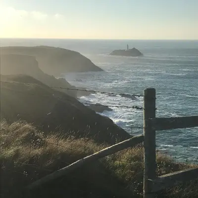 a fence in front of the ocean with a lighthouse at Stargazy Garden in Hayle