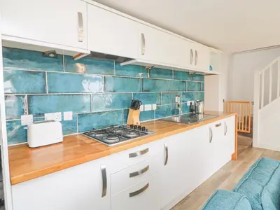 a kitchen with white cabinets and blue tiles at Leghorn in St Austell