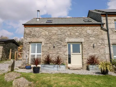 a stone house with a white door and some plants at Leghorn in St Austell