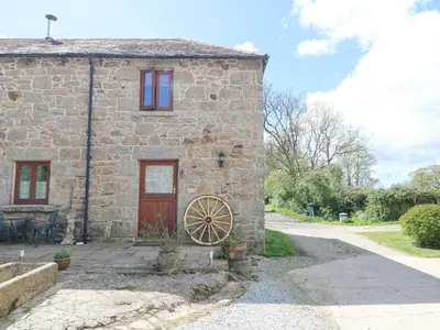 a stone house with a large wheel in front of it at Courtyard in Porthleven