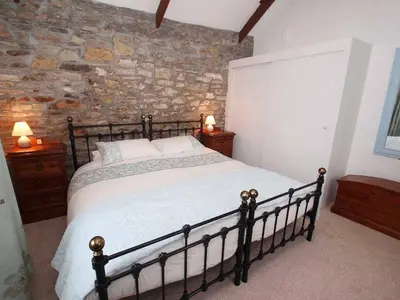 a bedroom with a large bed and a stone wall at Dairy Cottage in Bodmin