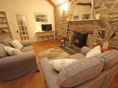 a living room with a couch and a stone fireplace at Dairy Cottage in Bodmin