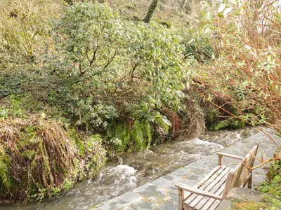 a wooden bench sitting on a stone path next to a stream at Millstream in Tintagel