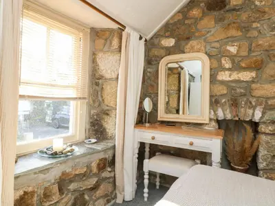 a stone walled bedroom with a vanity and a mirror at Pippin in St Ives