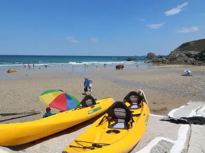 two yellow kayaks on a beach with people on the beach at Ocean Blue in Porthtowan