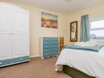 a bedroom with a bed and a dresser and a window at The Barn in Gunwalloe