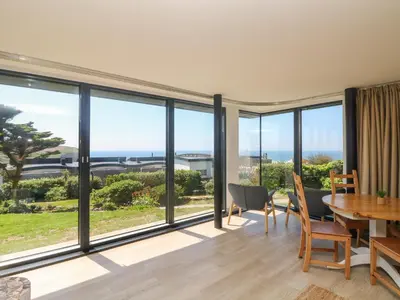 a living room with large windows and a table and chairs at Trelawns in Mawgan Porth