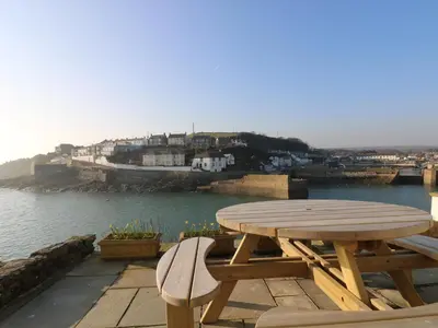 a wooden picnic table and chairs on a deck with the water at Haven in Helston