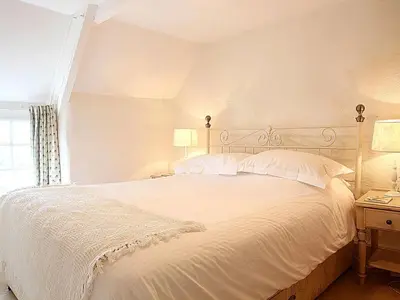 a bedroom with a large white bed and a window at Rose Cottage in Helston