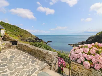 a stone staircase with pink flowers and the ocean at Kerbenetty Harbour Cottage in Portloe