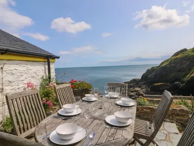 a wooden table with chairs and a view of the ocean at Kerbenetty Harbour Cottage in Portloe