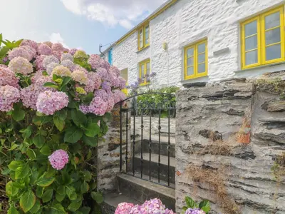 a white house with yellow windows and pink flowers at Kerbenetty Harbour Cottage in Portloe