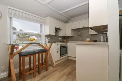 a kitchen with white cabinets and a table with stools at Higher Mount View in Marazion