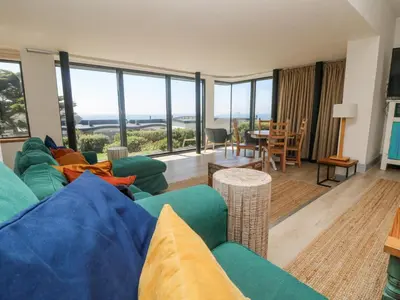 a living room with a blue couch and a view of the ocean at Little Trelawns in Mawgan Porth