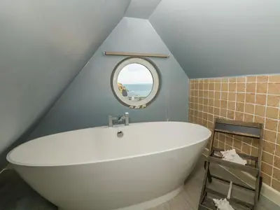 a bathroom with a large white tub in a attic at Little Trelawns in Mawgan Porth