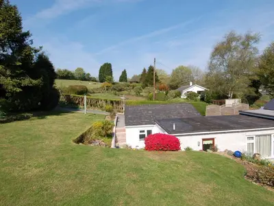 a white house with a red bush in the yard at Trevillas in St Austell