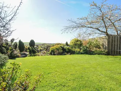 a yard with a green lawn with a fence and trees at Swallow Barn in Saint Kew