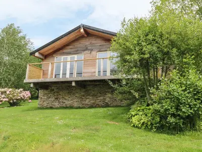 a wooden house on a lawn with a tree at 1 Lake View in Looe