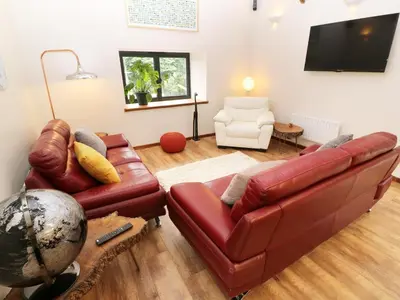 a living room with a leather couch and a television at The Cart House in Liskeard