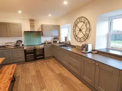 a kitchen with gray cabinets and a large clock on the wall at Silvermine House in St Austell