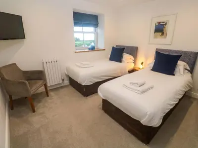 two beds in a room with a chair and a television at Silvermine House in St Austell