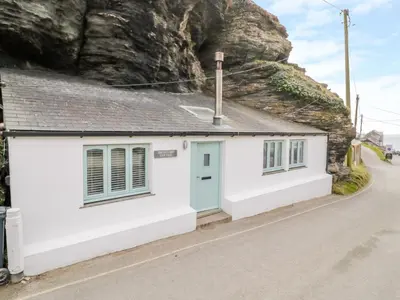 a white cottage with a blue door on the side of a road at Smugglers Cottage in Tintagel