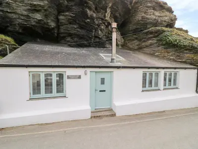 a white cottage with a blue door and a rock at Smugglers Cottage in Tintagel