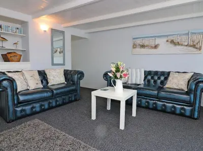 a living room with two black leather couches and a table at Pebble Cottage in Redruth