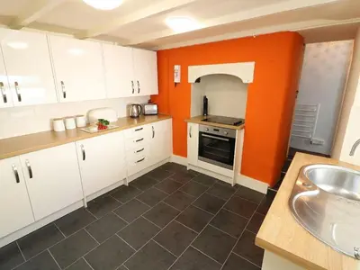 a kitchen with white cabinets and an orange wall at Pebble Cottage in Redruth
