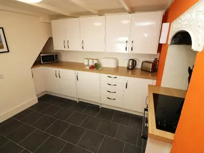 a small kitchen with white cabinets and a tile floor at Pebble Cottage in Redruth