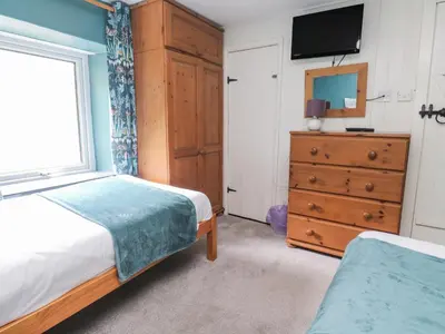a bedroom with a bed and a dresser and a television at Pebble Cottage in Redruth