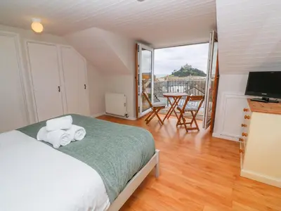 a bedroom with a bed and a balcony with a table at Mount View Cottage in Marazion