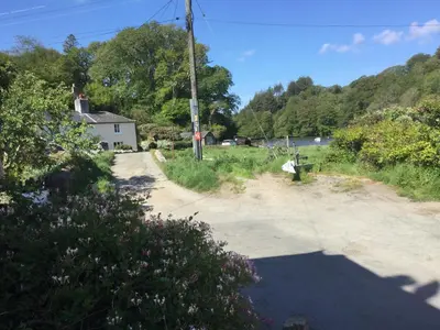 a dirt road next to a field with a house at Jasmine Cottage in Lerryn