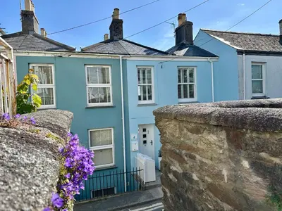 a blue house with a stone wall and purple flowers at Jacob's View in Falmouth