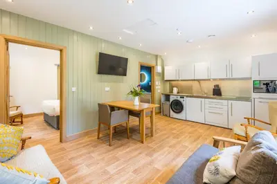 a living room with a table and a kitchen at Pinetum Garden Cottages in St Austell