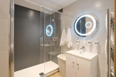a bathroom with a shower and a sink and a mirror at Pinetum Garden Cottages in St Austell