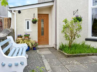 a white bench in front of a house with a door at Bay Cottage in Par