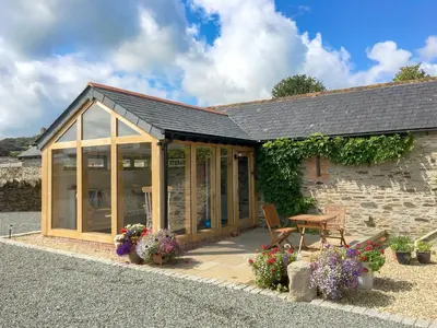 a house with a conservatory with flowers in front of it at Trezeal Barn in North Hill