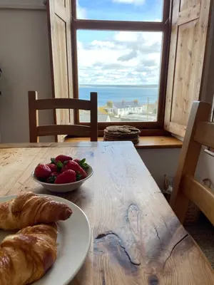 a table with a plate of bread and a bowl of fruit at Huers Watch Beautiful Apartment with Panoramic Views over St Ives Bay and private parking in St Ives