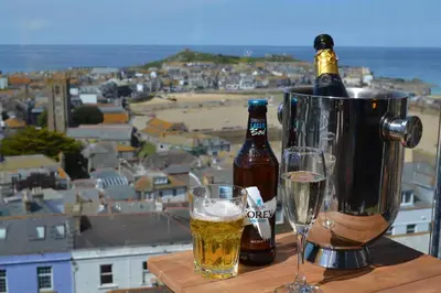 two bottles of beer and glasses on a table with a city at THE PENTHOUSE Top Floor Apartment with Bay Views, Large Balcony & Onsite Parking in St Ives