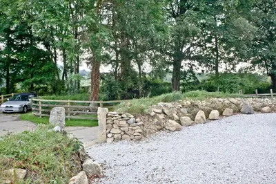 a fence and a stone wall with a car in a field at The Barn in Lanhydrock, Bodmin in Bodmin