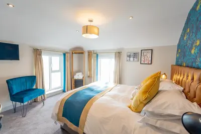 a bedroom with a large bed and a blue chair at The Inn on the Shore in Torpoint