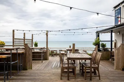 a wooden deck with tables and chairs and the ocean at The Inn on the Shore in Torpoint
