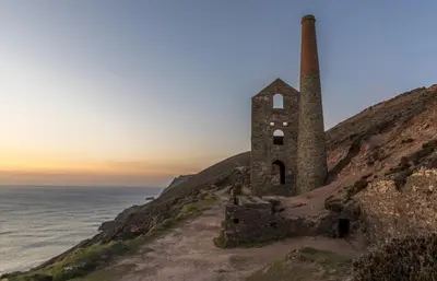 an old building on a hill next to the ocean at Beacon Country House B & B & Luxury Shepherd Huts in St. Agnes