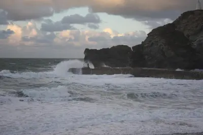 a beach with waves and a lighthouse in the ocean at Inner Harbour Cottage in Portreath