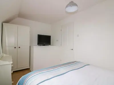 a white bedroom with a bed and a tv at Sarah's Cottage in Padstow